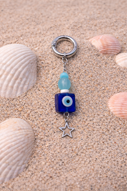 Keychain with blue eye charm and star pendant on sand with shells