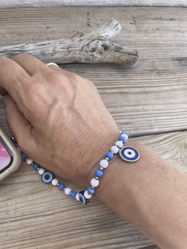 Hand wearing a blue and white beaded bracelet on a wooden surface with driftwood.