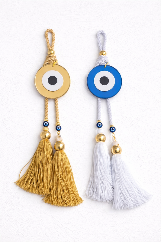 Two evil eye charms with tassels, one gold and one white, on a white background.