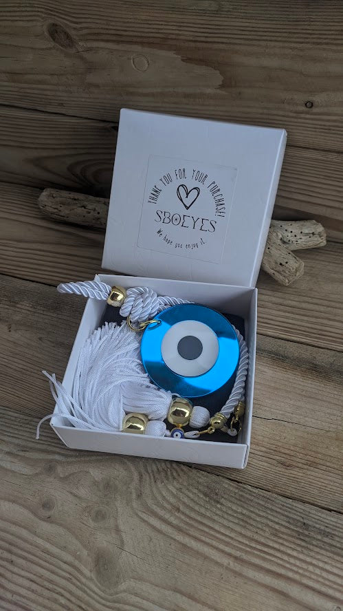 Blue evil eye charm with white string in a white box on a wooden surface
