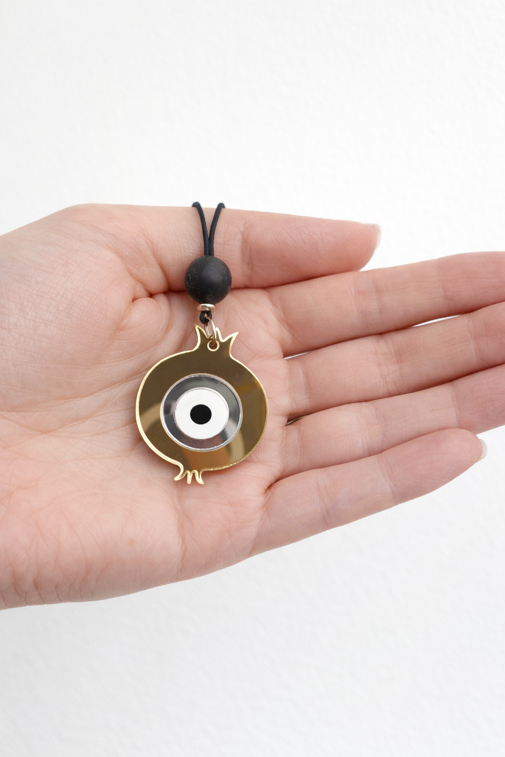 Hand holding a gold and silver pendant with a black cord against a white background