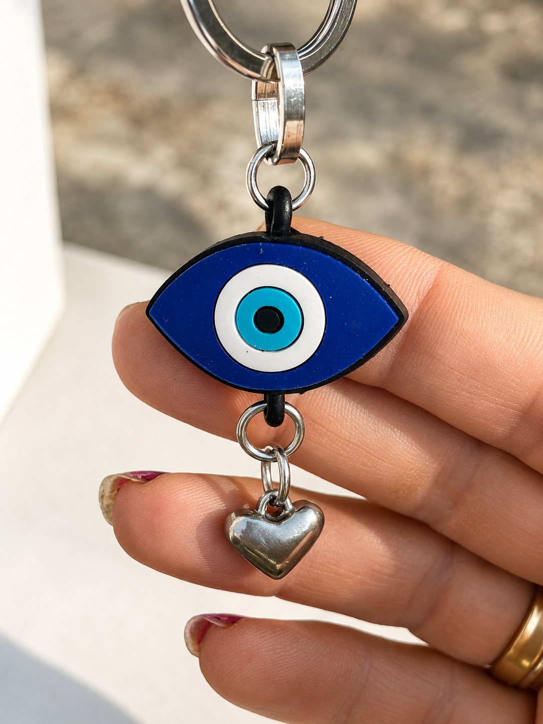 Handmade Greek evil eye bag charm held by hand with the Mediterranean Sea in the background.