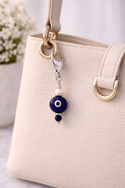 Beaded keychain with blue evil eye charm attached to a beige handbag.