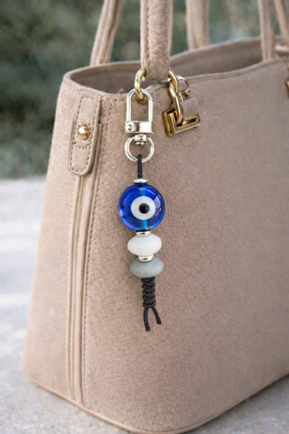 Beaded keychain with blue evil eye charm attached to a beige handbag.