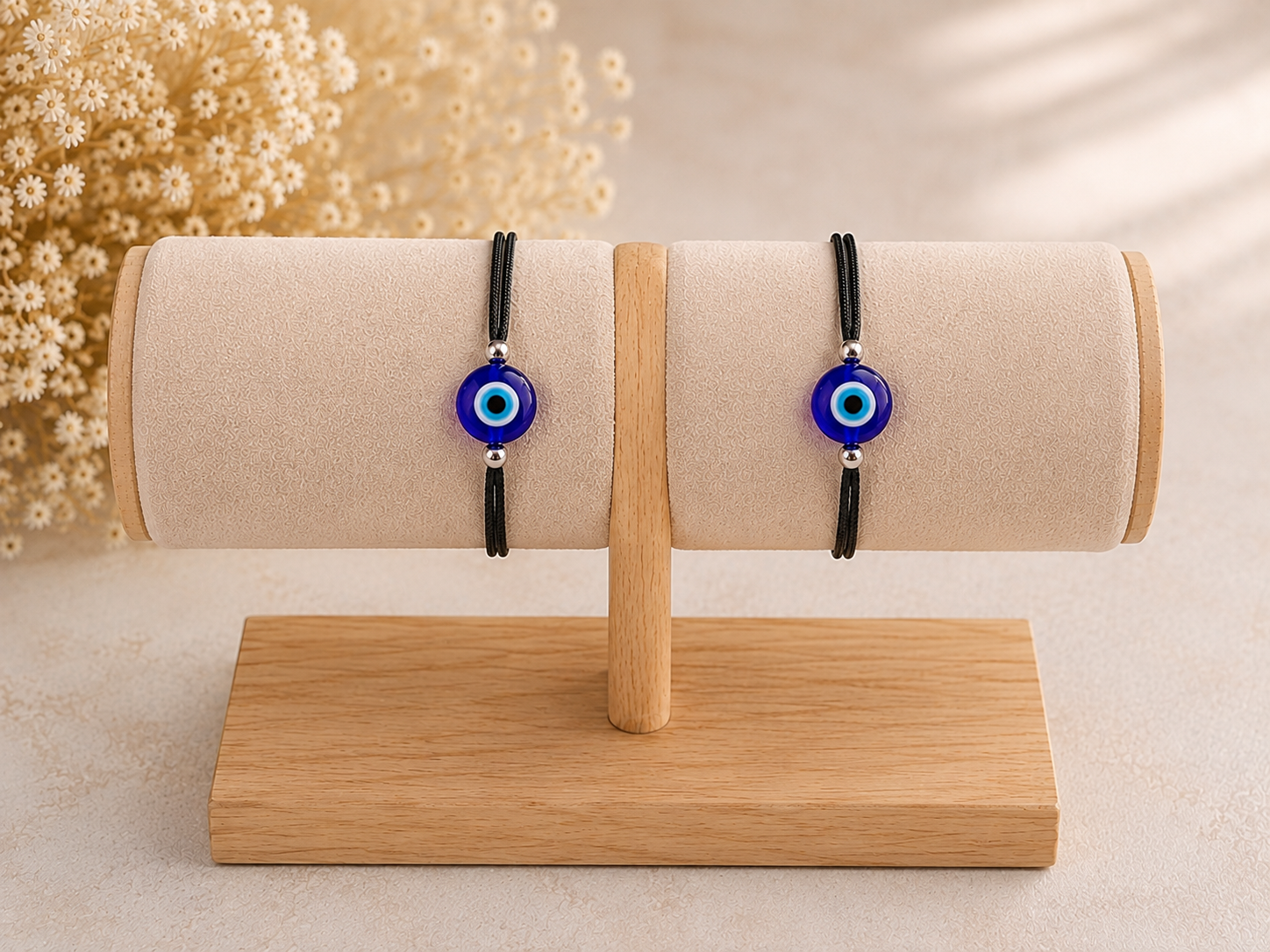 Two black cord bracelets with blue and white evil eye beads displayed on a beige fabric jewelry roll stand on a wooden base.