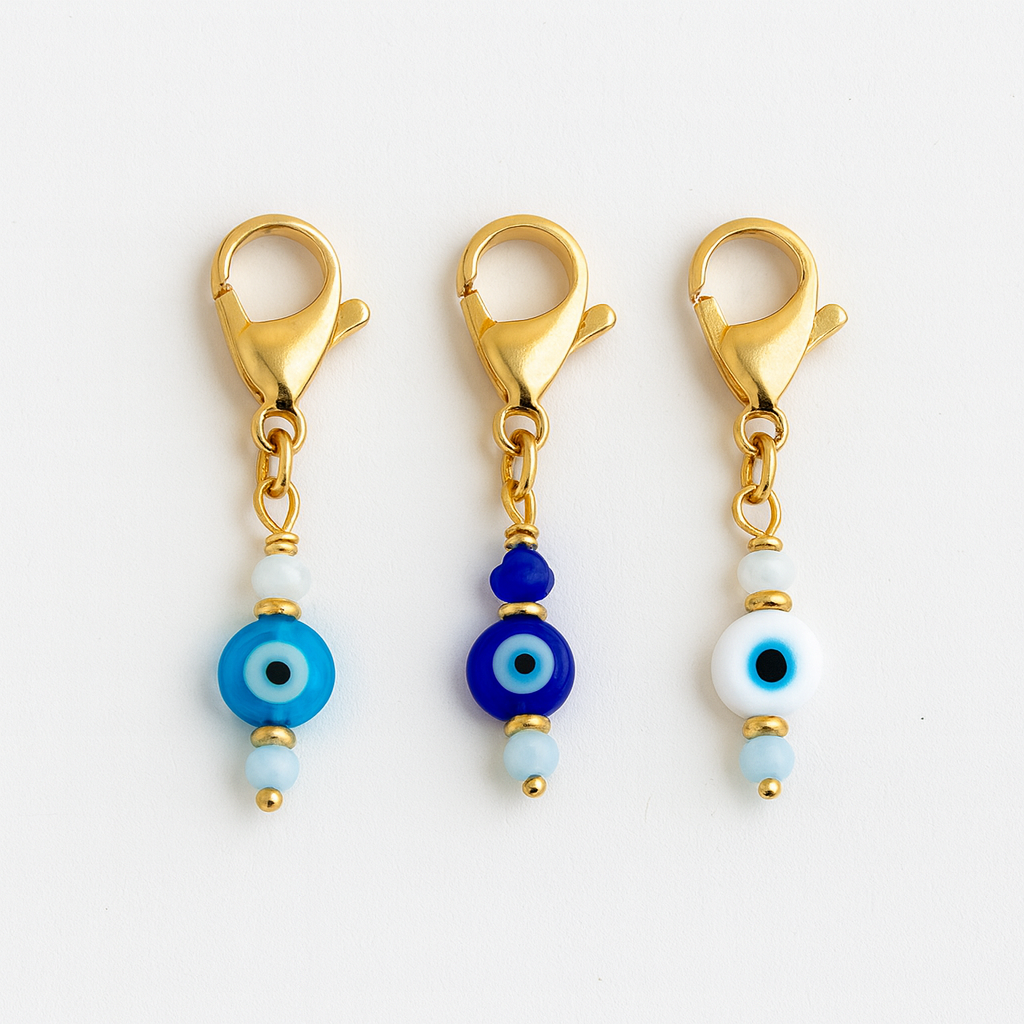 Three gold charm clips with blue and white evil eye beads on a white background