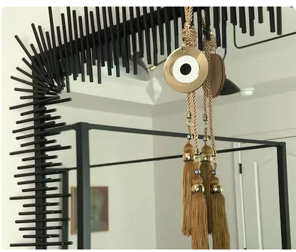 Decorative wall art with black geometric design and gold evil eye and tassels.