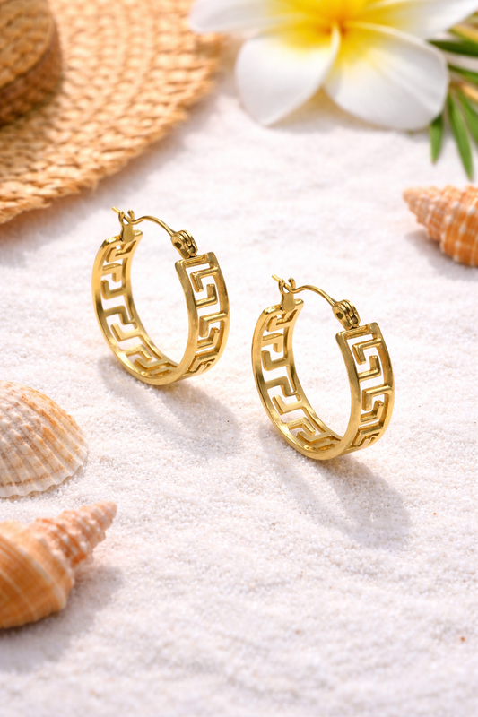 Gold hoop earrings on a sandy surface with shells and flowers