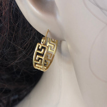 Gold hoop earrings with a detailed design worn on an ear.
