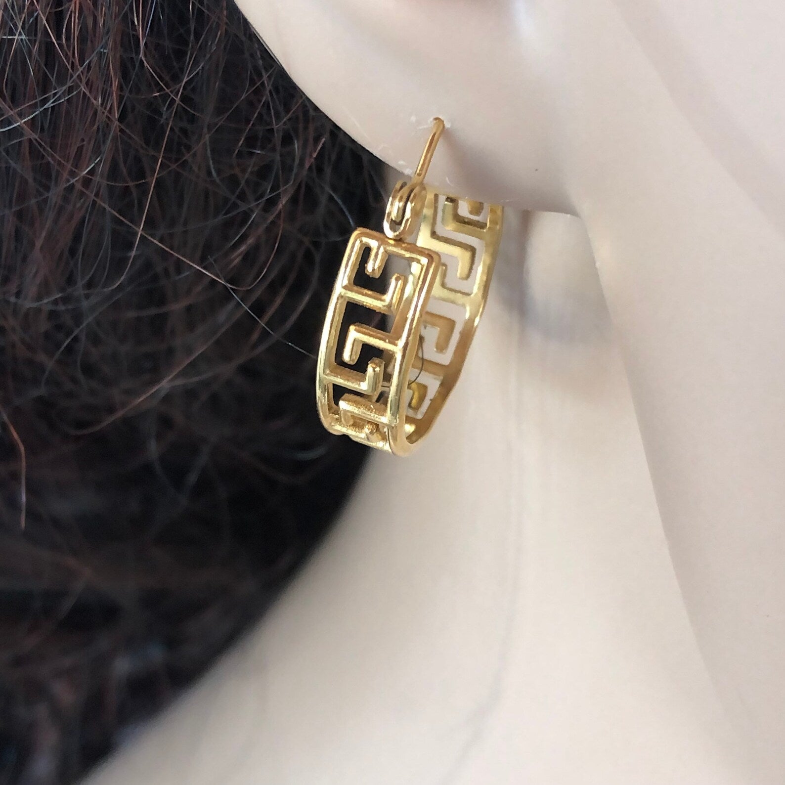 Gold hoop earring worn on an ear with a neutral background