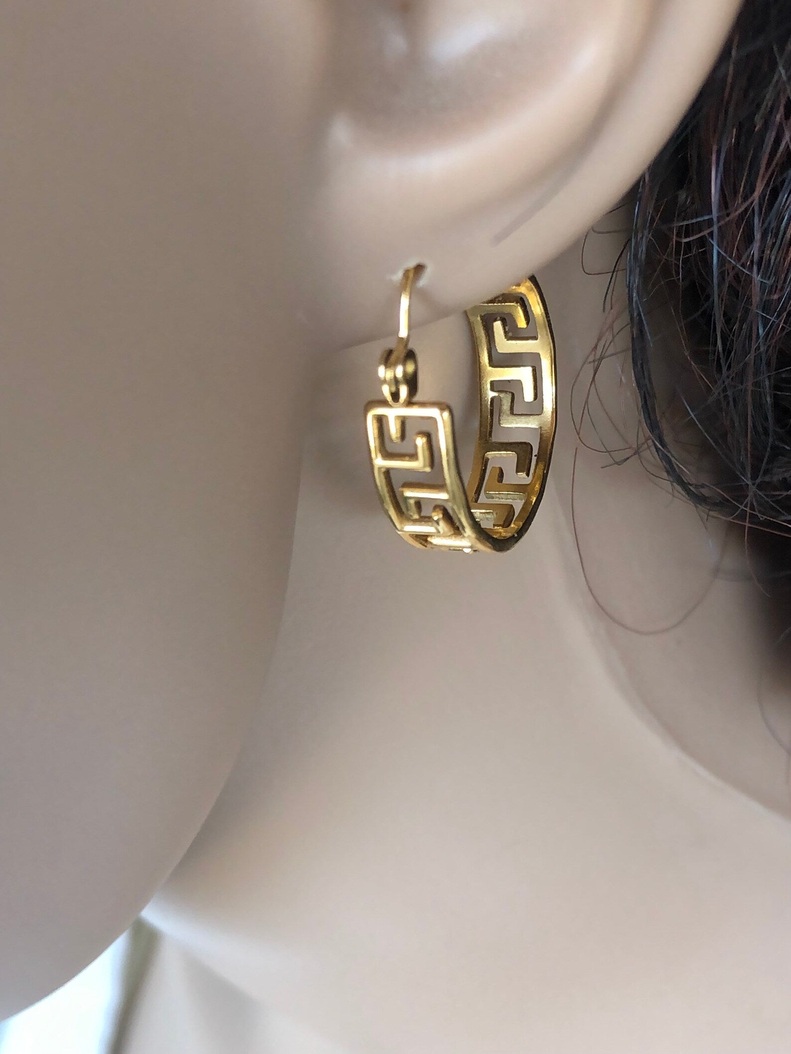 Gold hoop earrings on a mannequin ear with a neutral background