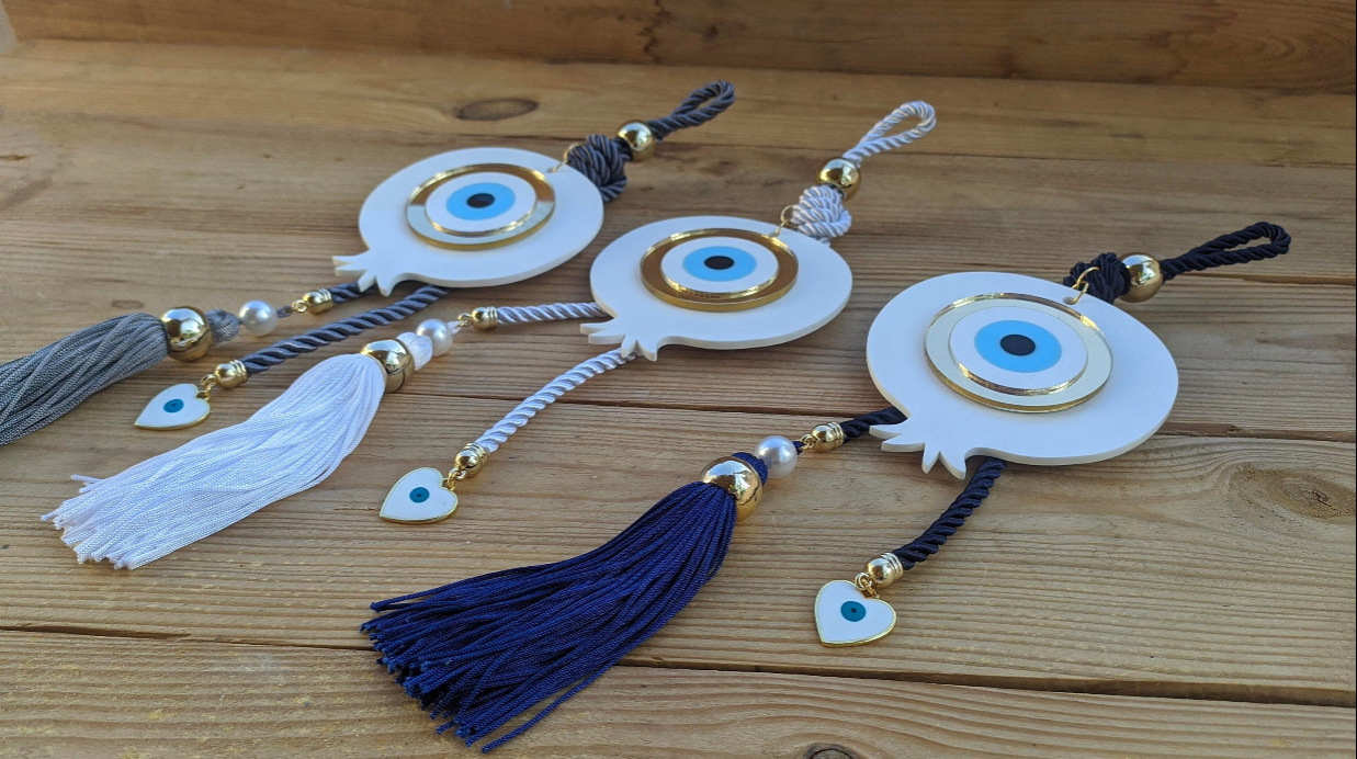 Handmade Greek evil eye pomegranate ornament with a white tassel and heart charm, designed as a meaningful housewarming and home blessing gift.
