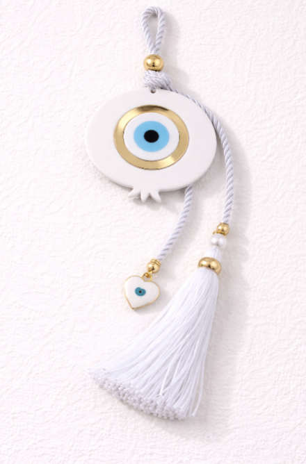 Handmade white plexiglass wall hanging featuring a Greek evil eye, pomegranate design, white tassel, and small heart charm for protection, luck, and prosperity.