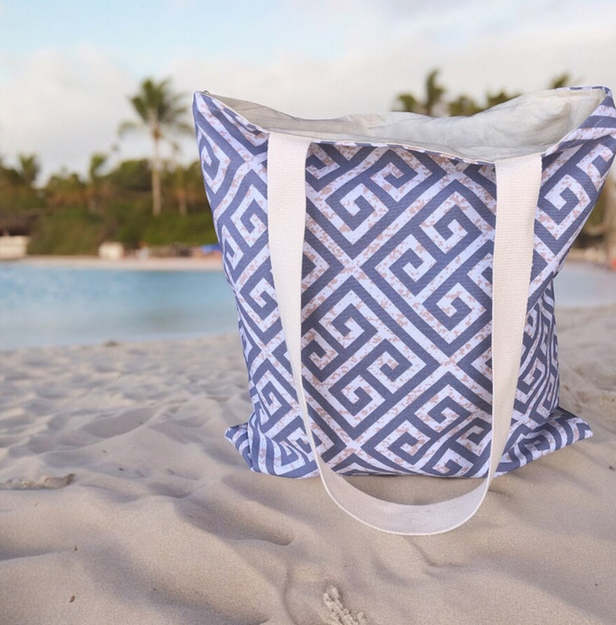 Grey cotton tote bag with a blue Greek key pattern displayed on a wooden chair in a bright Mediterranean-inspired interior.