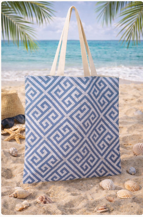 Blue and white patterned tote bag on a sandy beach with ocean and palm leaves in the background