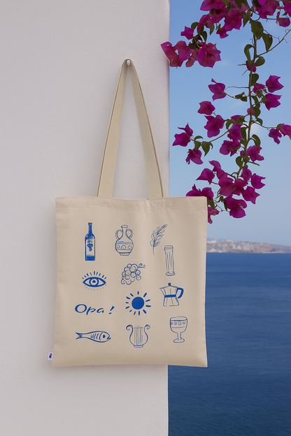 Beige tote bag with blue illustrations against a scenic background with flowers and water.