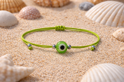 Green bracelet with a green eye bead on sand with shells