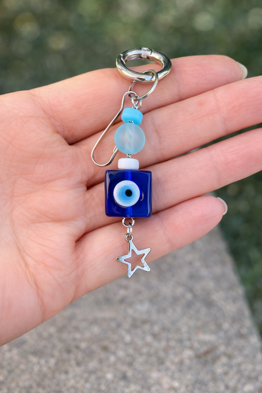 Hand holding a blue evil eye charm with star and bead details.