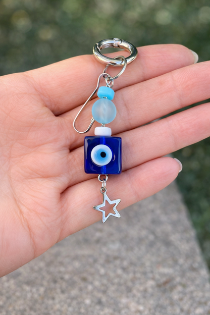 Hand holding a blue evil eye charm with star and bead details.