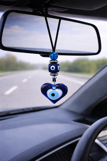 Car rearview mirror with a blue heart-shaped evil eye ornament.