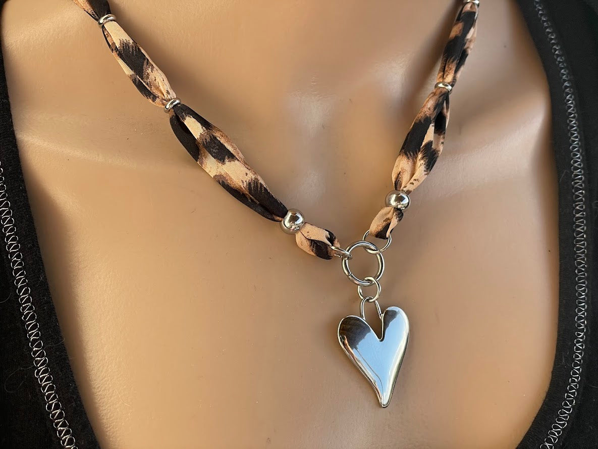 A leopard print fabric strap necklace with a heart-shaped charm and a stainless steel clasp.