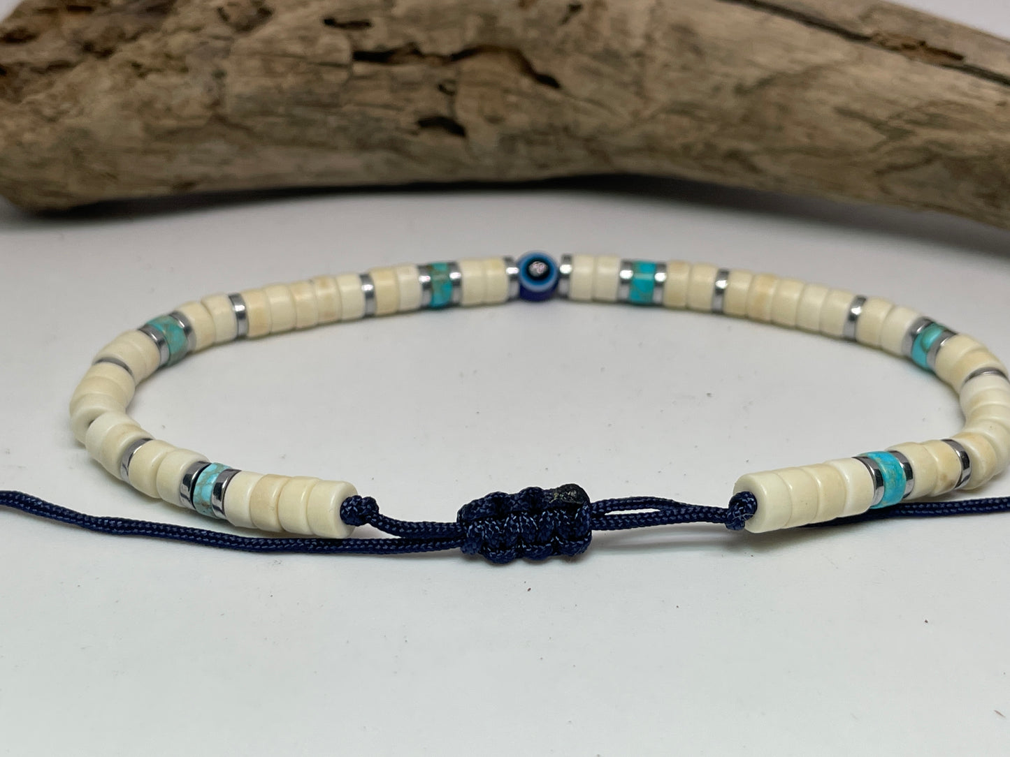 Beaded necklace with blue cord on a white surface with driftwood in the background