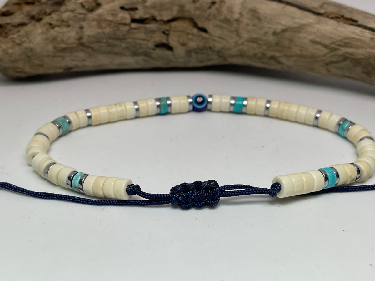 Beaded necklace with blue cord on a white surface with driftwood in the background