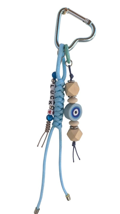 A handbag charm featuring a silicone evil eye, wooden beads, and a blue cord attached to a handbag.