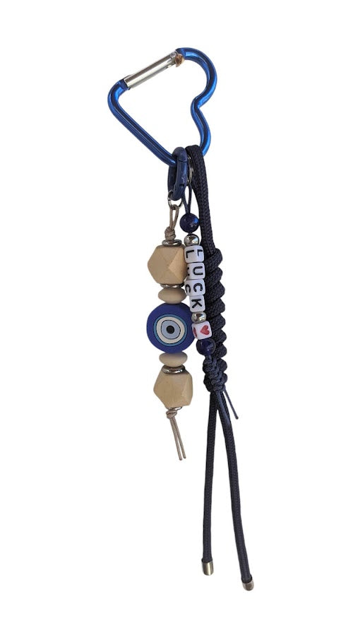 A handbag charm featuring a silicone evil eye, wooden beads, and a blue cord attached to a handbag.