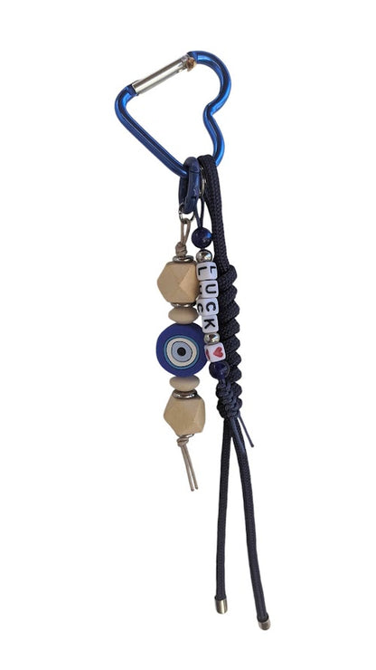 A handbag charm featuring a silicone evil eye, wooden beads, and a blue cord attached to a handbag.