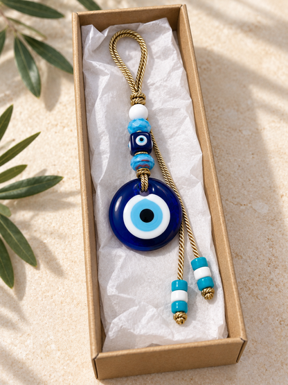 An evil eye wall hanging charm lies inside an open brown cardboard gift box lined with white tissue pape