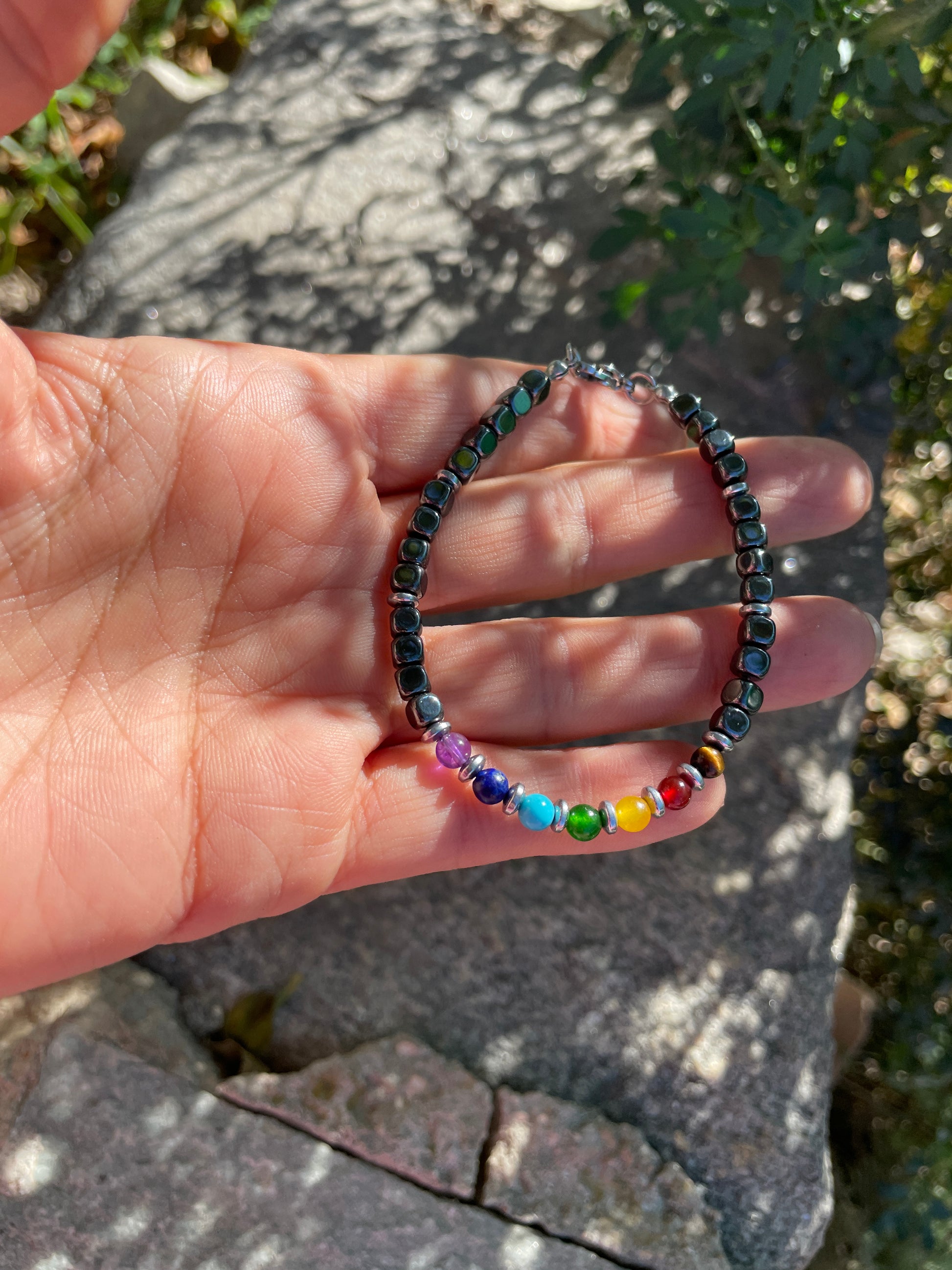 Hand holding a colorful beaded bracelet with a natural stone background
