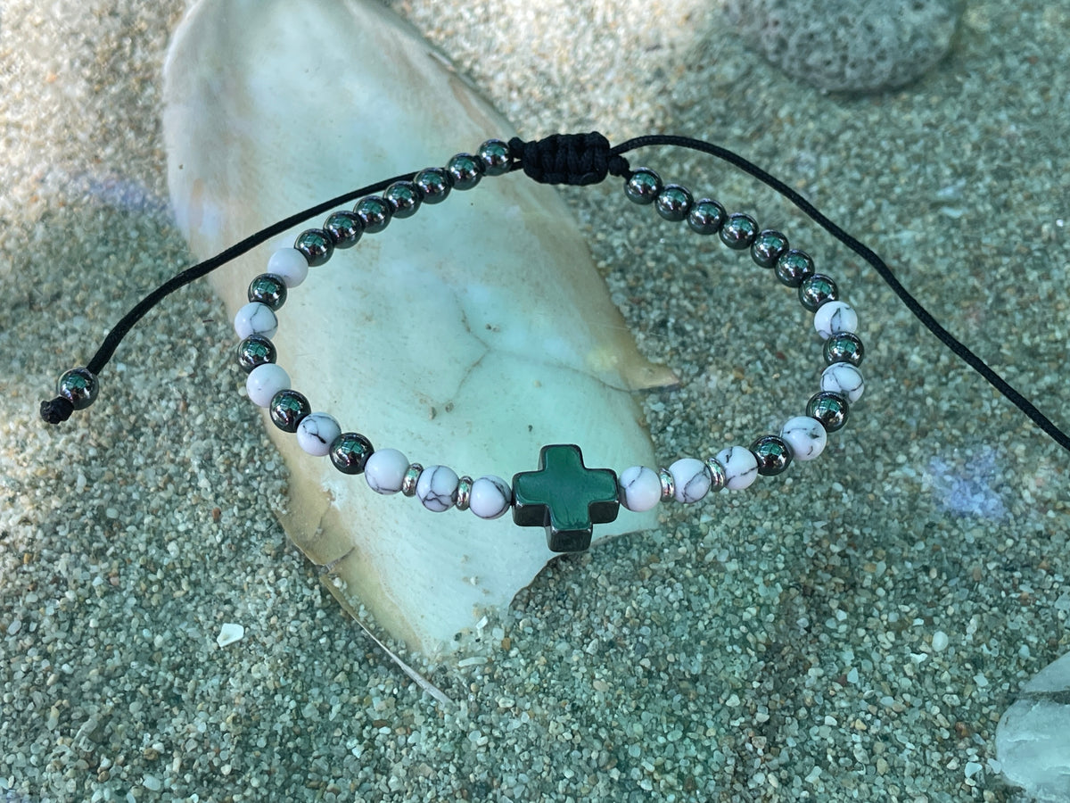 Bracelet with a green cross charm on a stone surface