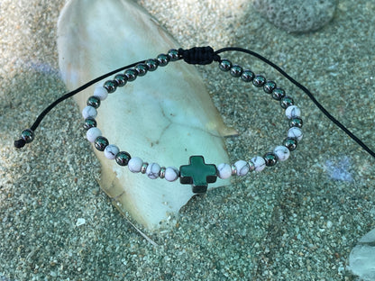 Bracelet with a green cross charm on a stone surface