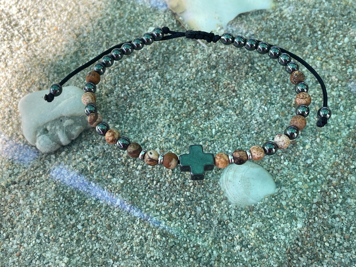 Beaded bracelet with a cross charm on a sandy surface