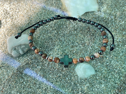 Beaded bracelet with a cross charm on a sandy surface