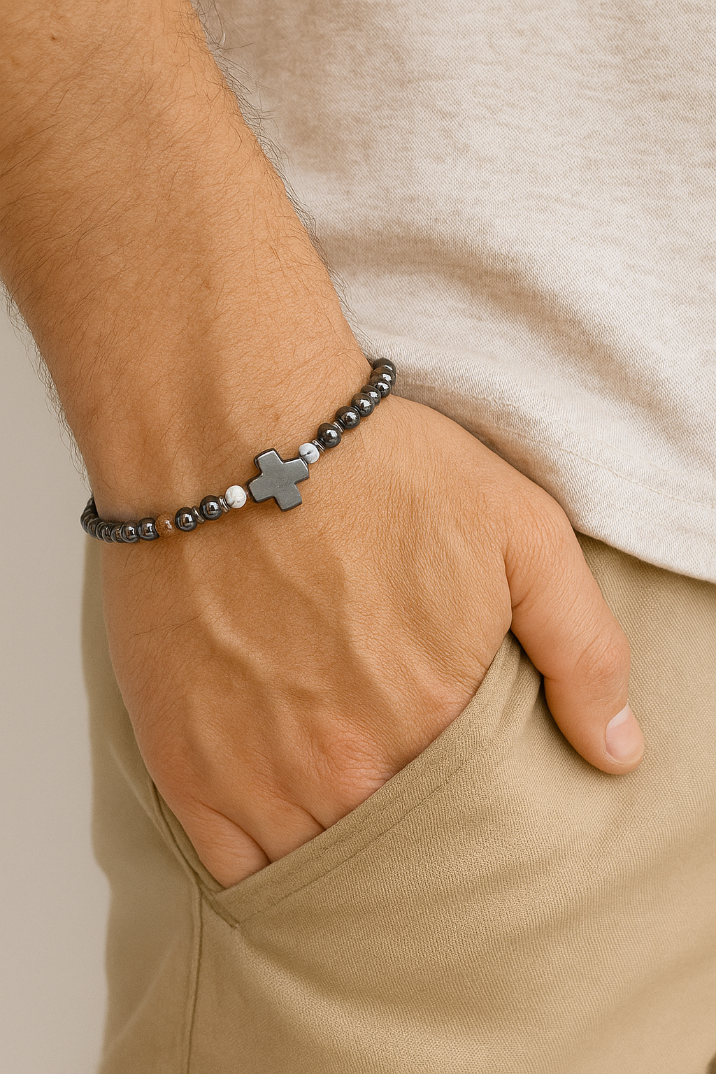 Hand wearing a bracelet with a cross charm on a neutral background