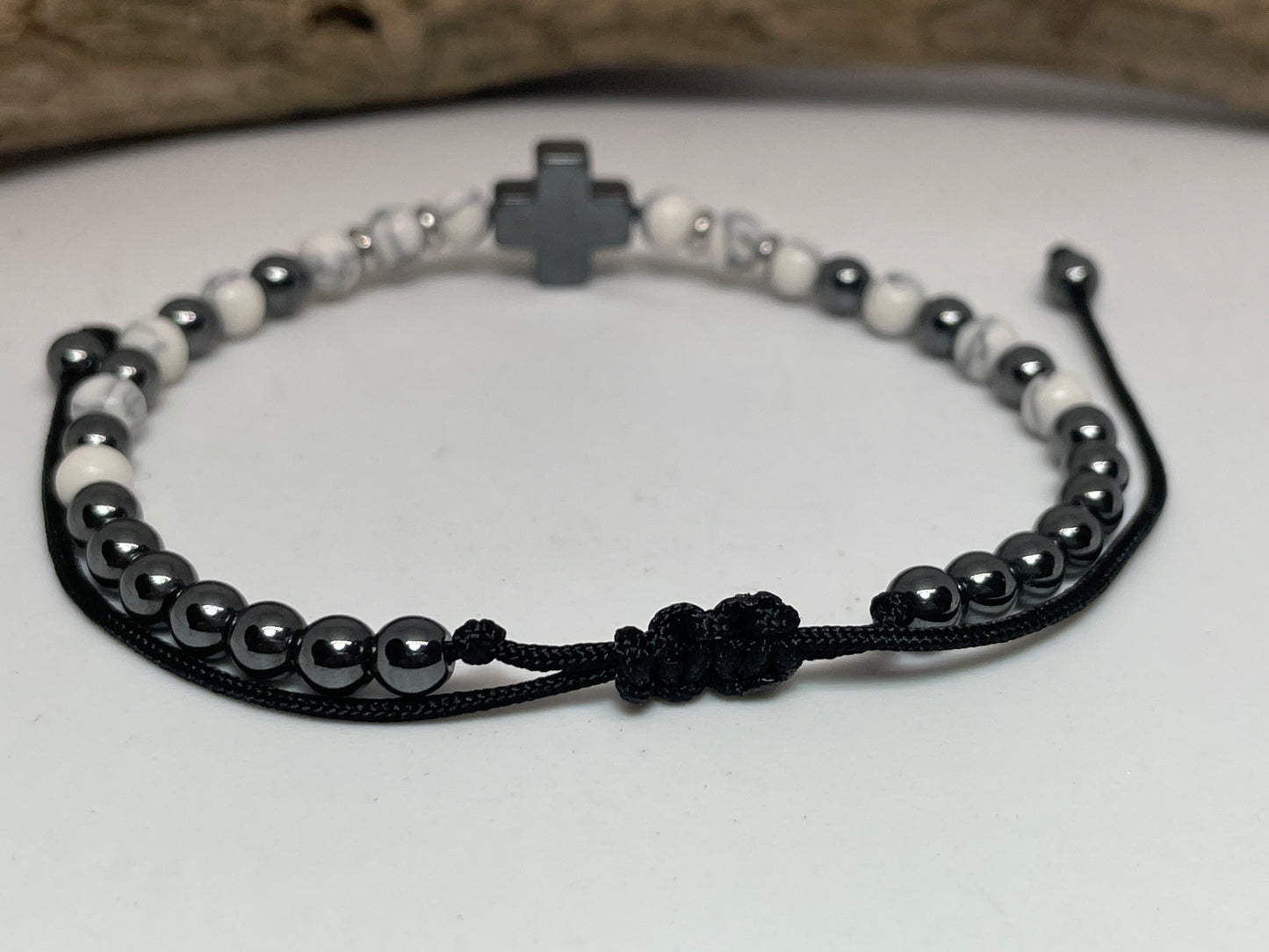 Bracelet with black and white beads and a cross charm on a light background