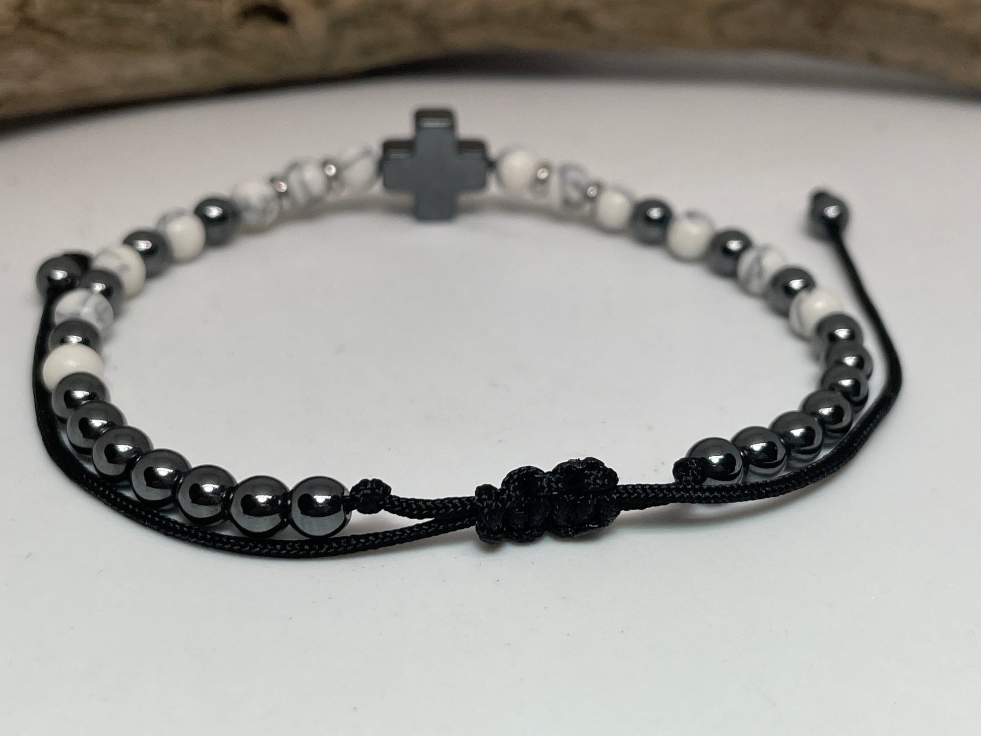 Bracelet with black and white beads and a cross charm on a light background