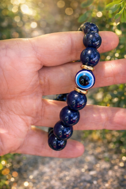 Hand holding a blue beaded bracelet with an eye charm against a blurred natural background
