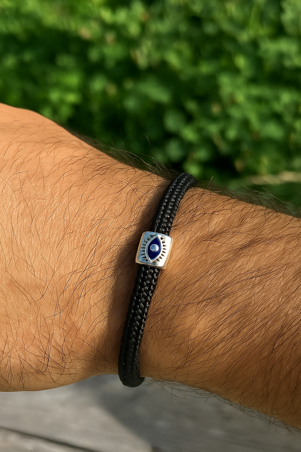 Black braided bracelet with a silver clasp on a wrist against a blurred green background