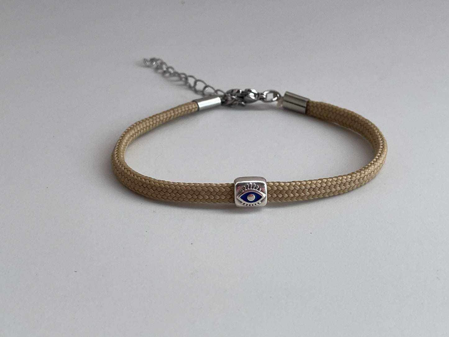 Beige braided bracelet with a silver clasp and eye charm on a light gray background
