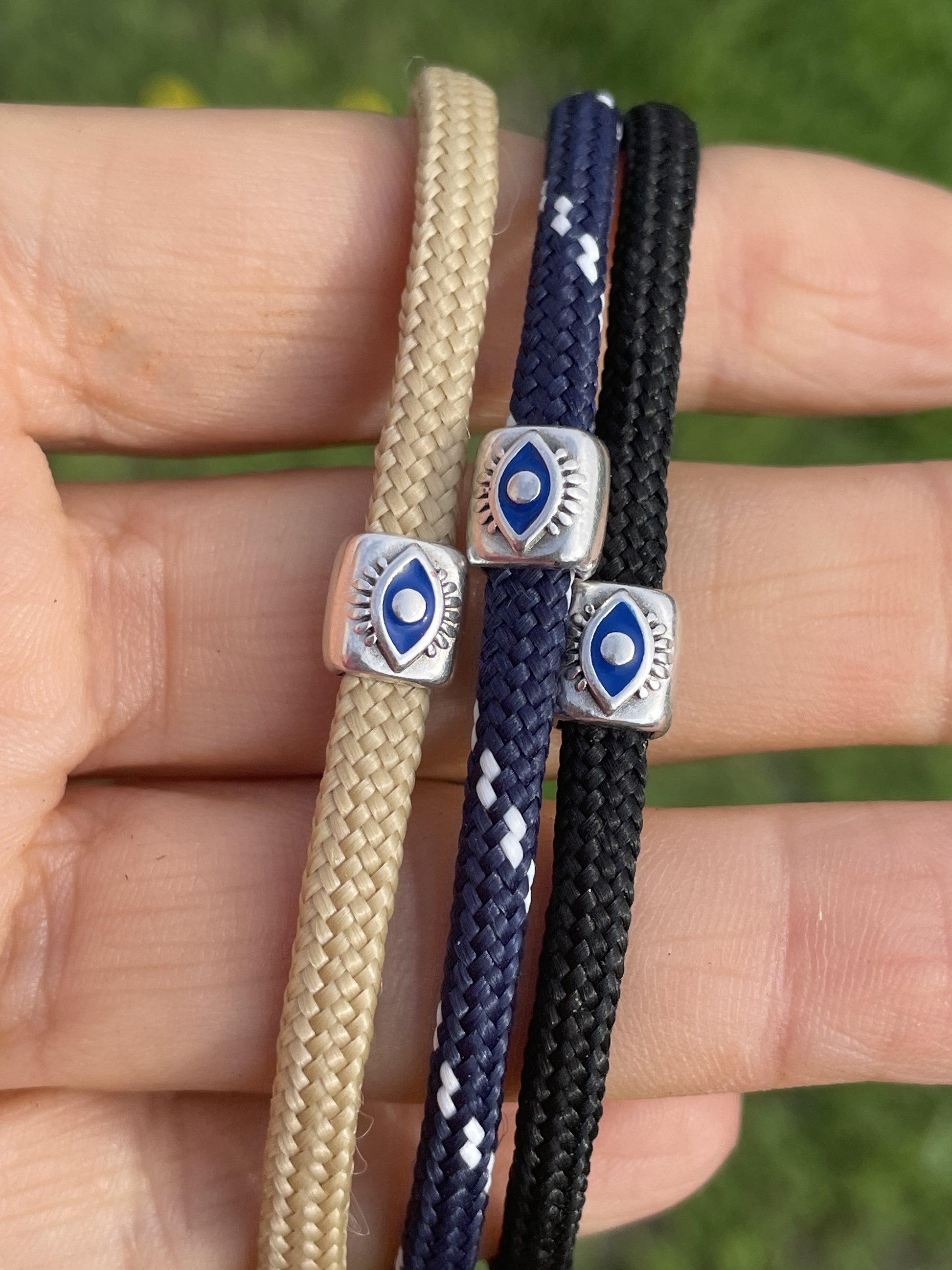 Three braided bracelets with metal ends held in a hand against a blurred green background