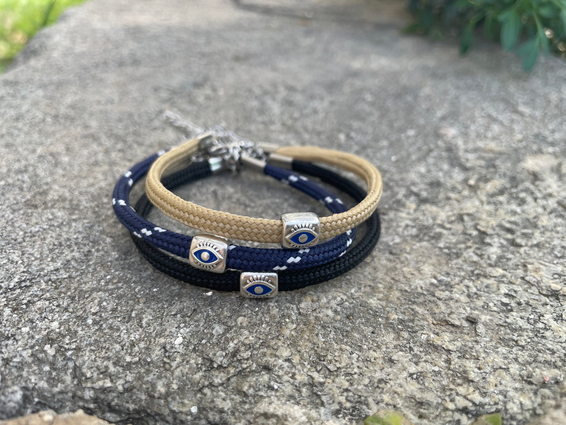 Three layered bracelets with evil eye charms on a stone surface