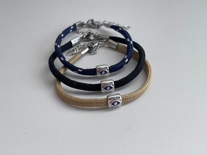 Three braided bracelets with evil eye charms on a light gray background