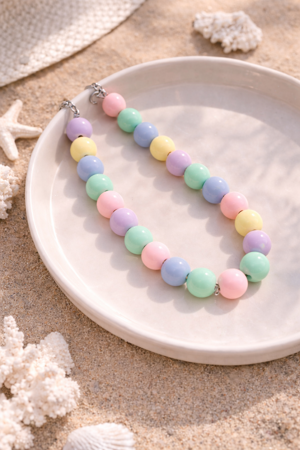 Pastel bead necklace on a white plate with seashells and coral in the background