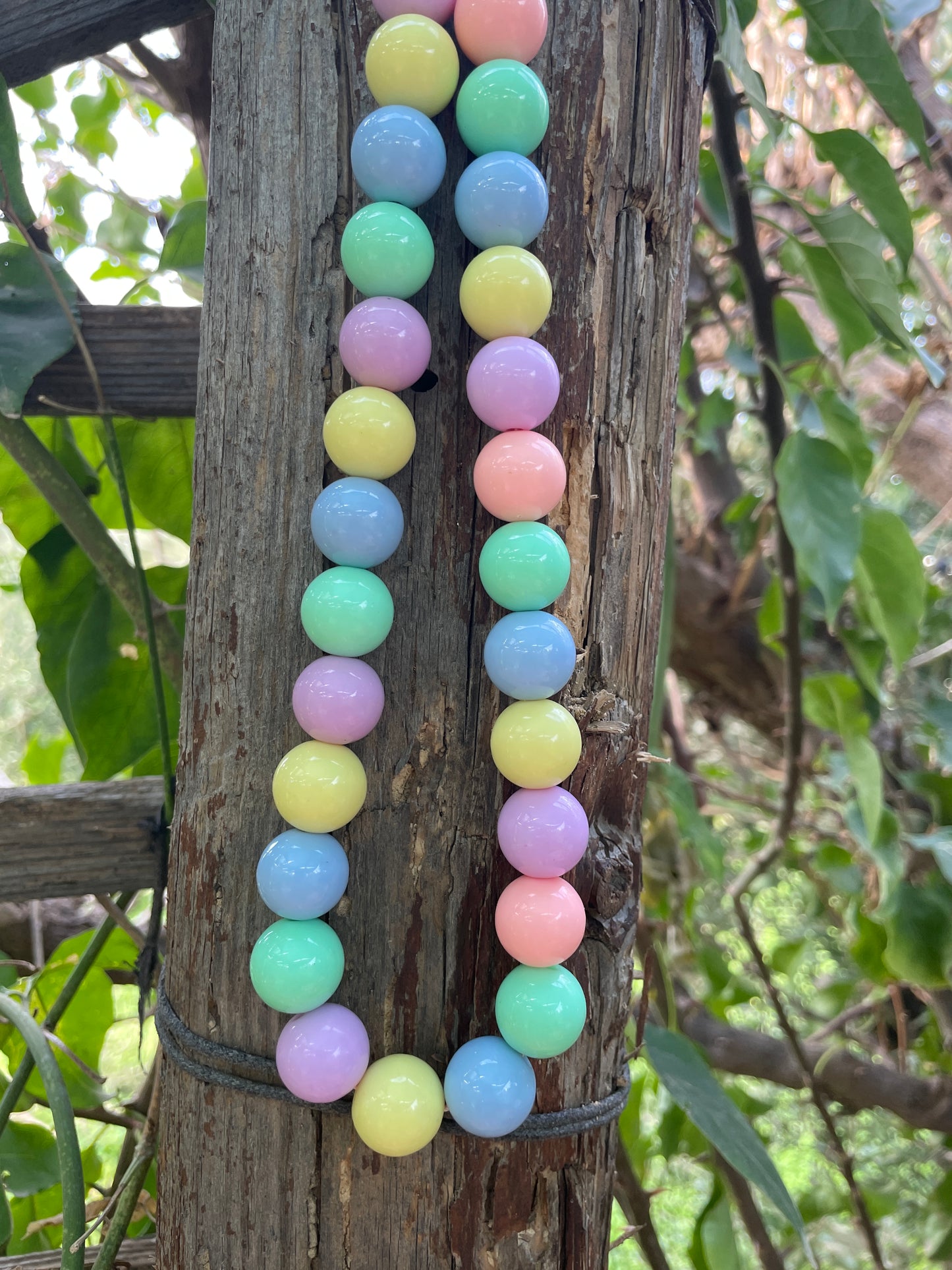 Pastel-colored beads on a wooden log with green foliage in the background