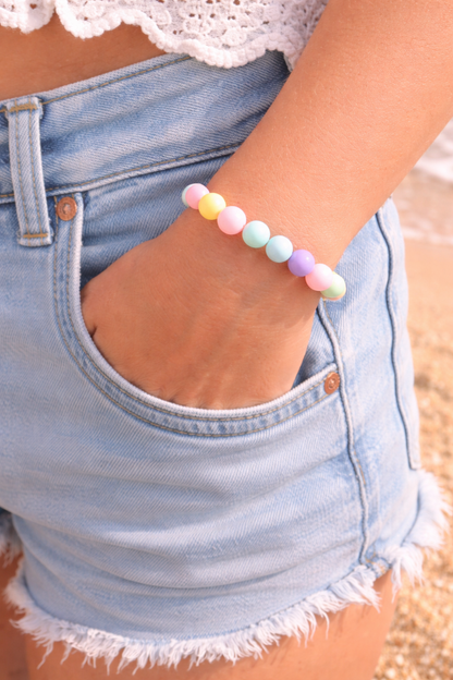 Pastel beaded bracelet on a person wearing denim shorts with a blurred beach background