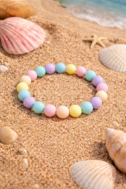 Pastel beaded bracelet on a sandy beach with shells and starfish.