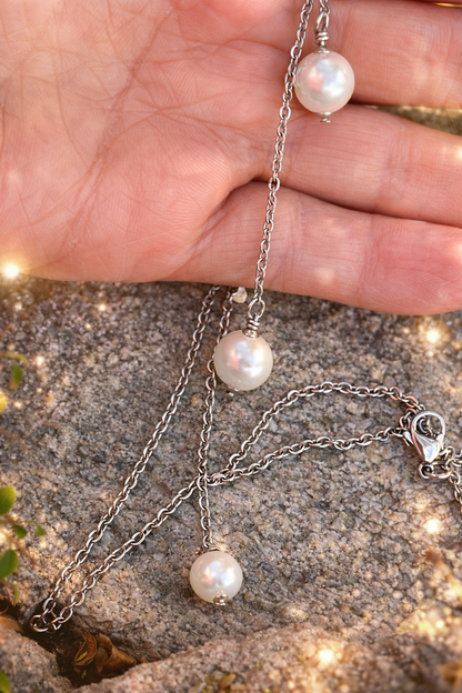 Pearl necklace with silver chain held over a textured surface